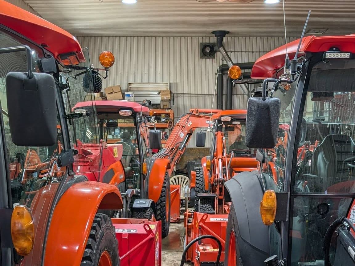 Intérieur du garage de l'entreprise : plusieurs tracteurs Kubota alignés dans une allée, avec leurs souffleuses et leurs godets attelés